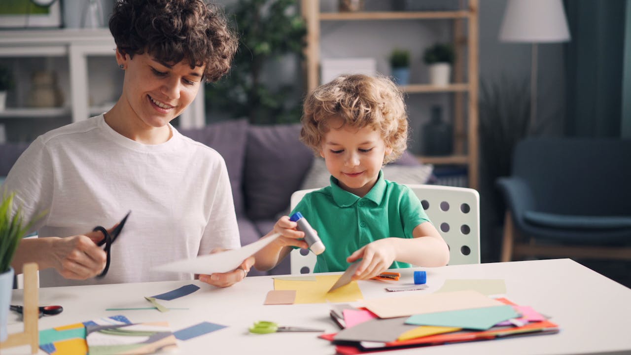 A joyful mother and son bond over crafting with paper and scissors at home.