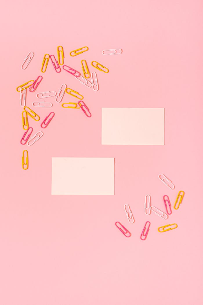 Top view of colorful paper clips scattered on a pink background with blank cards.